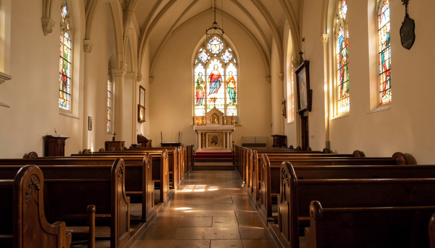 Warm interior of a Catholic church with wooden pews, soft amber light filtering through stained glass, and a quiet reverent atmosphere