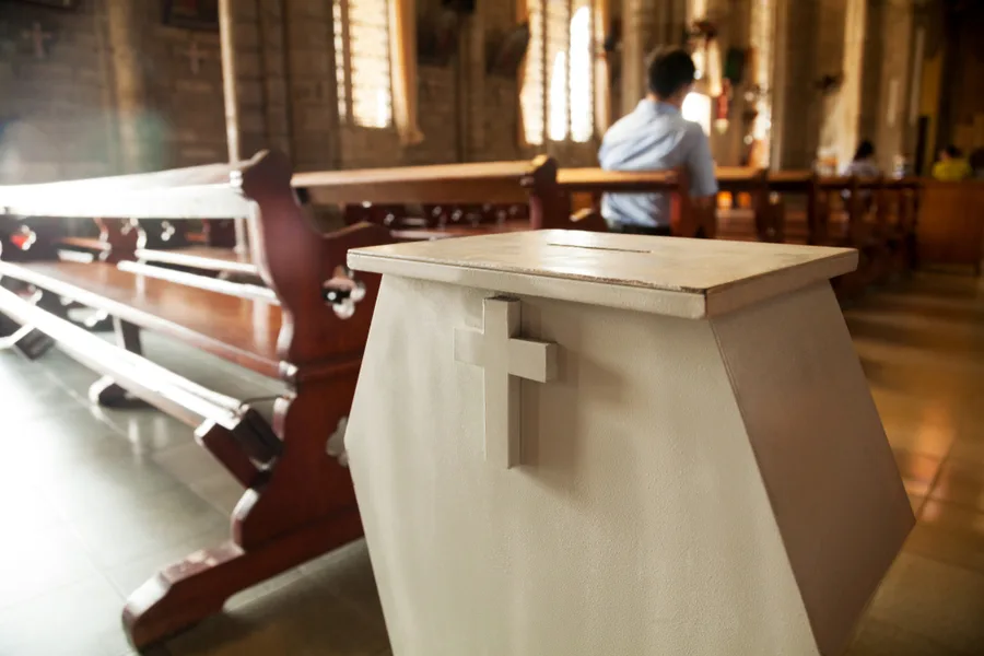 Interior of a church with wooden pews, a small cross-decorated box in the foreground, soft light, quiet contemplative mood